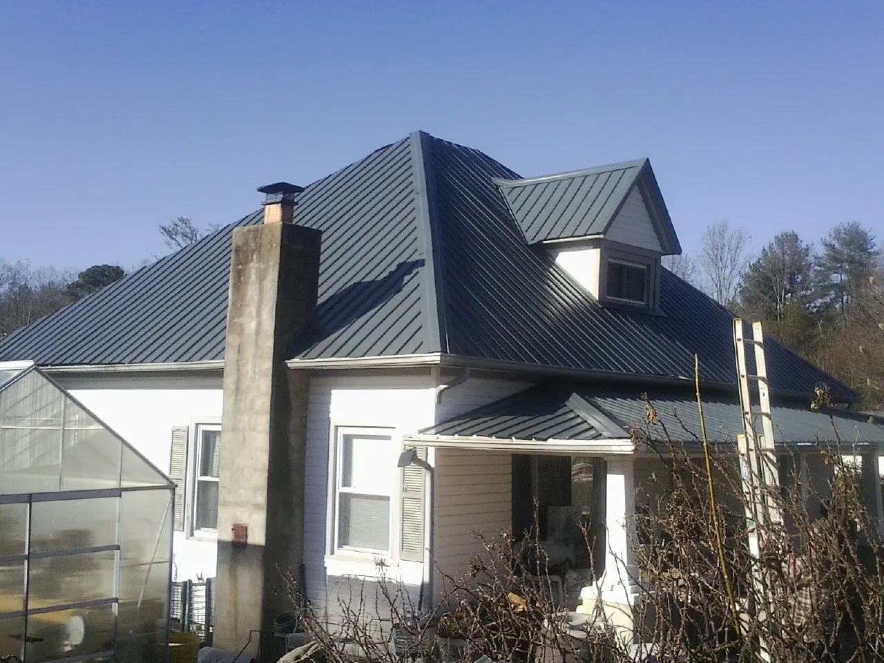 Dark blue standing seam metal roof on a white farmhouse with dormer — Slate & Tile Roof Repair by Roofing Brothers in Pantego