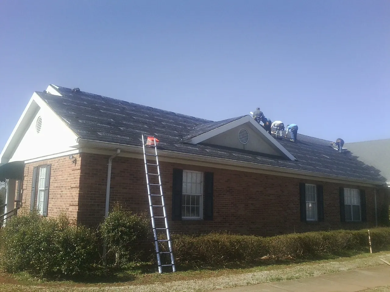 Crew tearing shingles off a brick ranch roof with a ladder set — Emergency Roof Repair work by our crew in Pantego