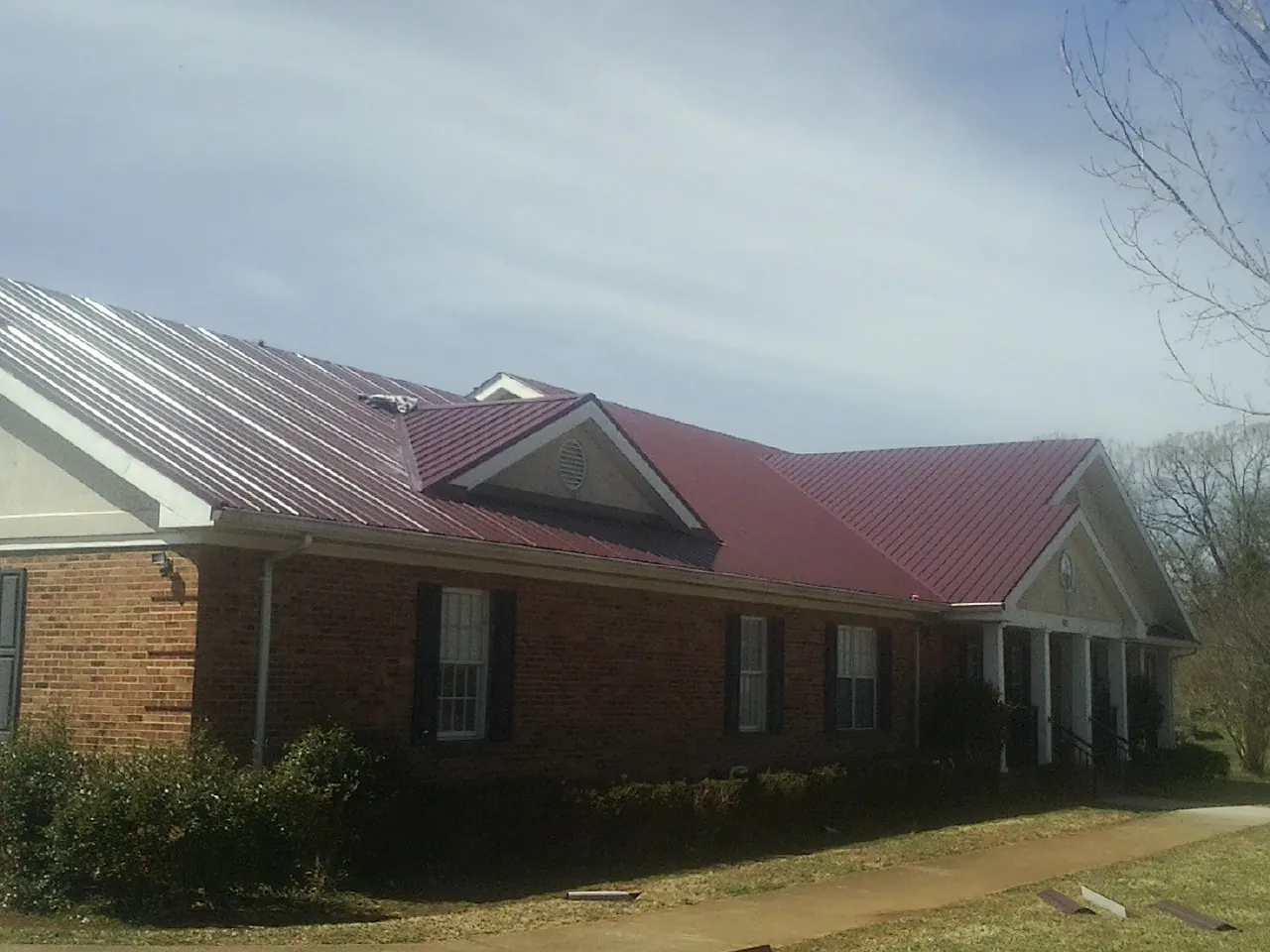 Red metal roof with gabled entries on a long brick building, from a Hail Damage Roof Repair job in Pantego