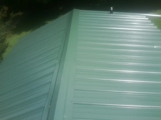 New green metal panels meeting at the ridge of a roof — Flat Roof Repair work by our crew in Pantego