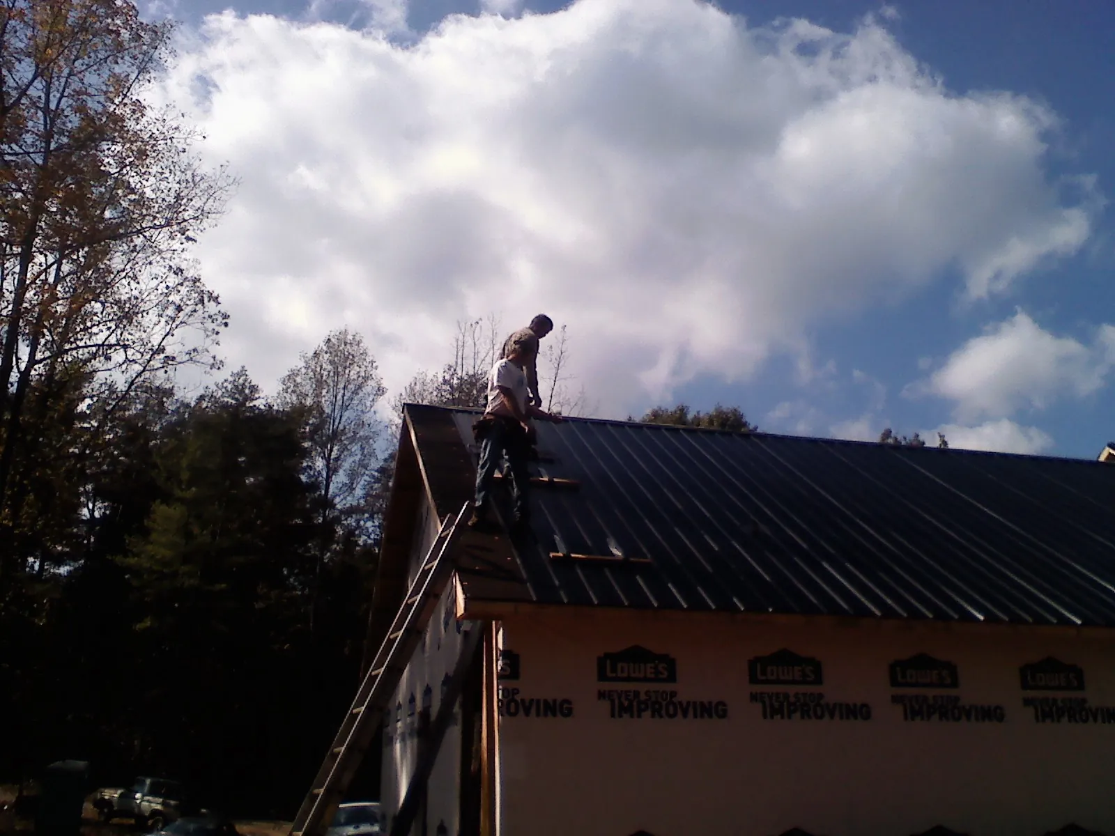 Roofer fastening dark metal panels high against a cloudy sky, from a Roof Inspection job in Pantego