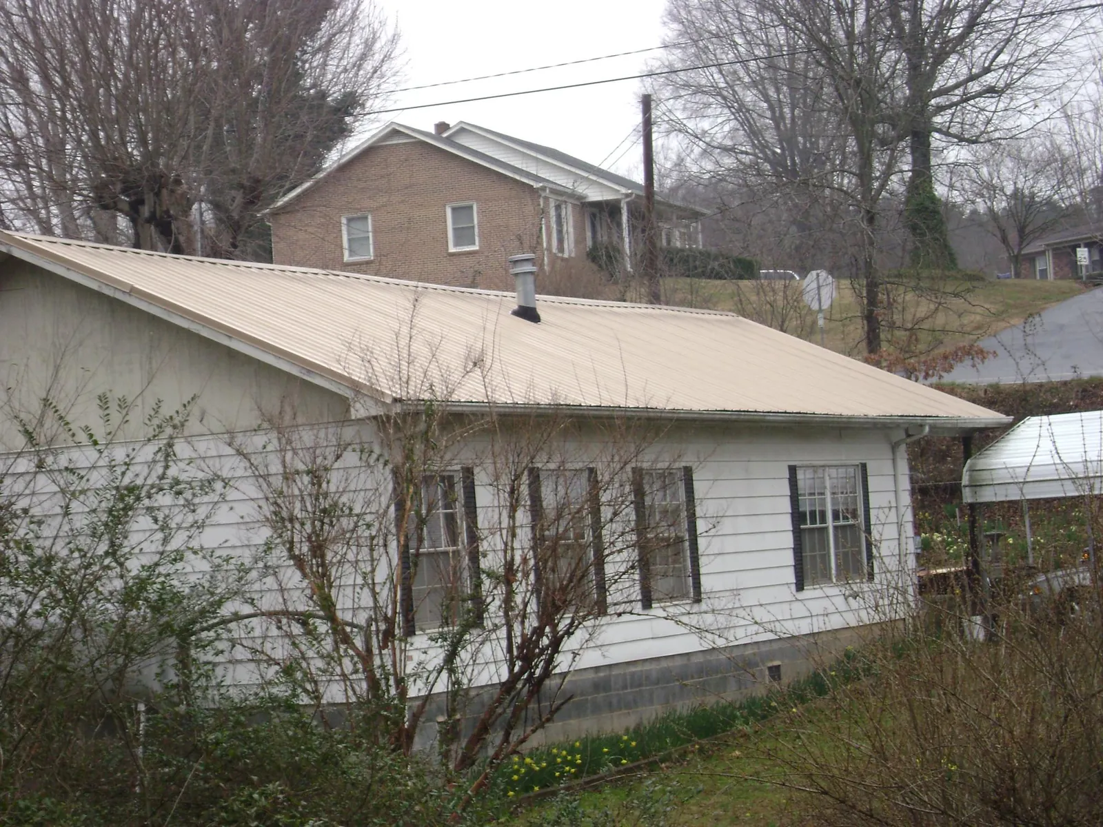 Tan metal roof on a white sided house set into a hillside — Commercial Roofing by Roofing Brothers in Pantego